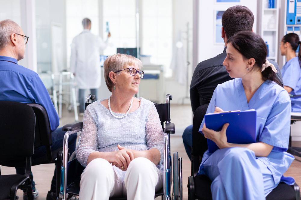 nurse filing documents while talking with disabled senior woman in hospital waiting area