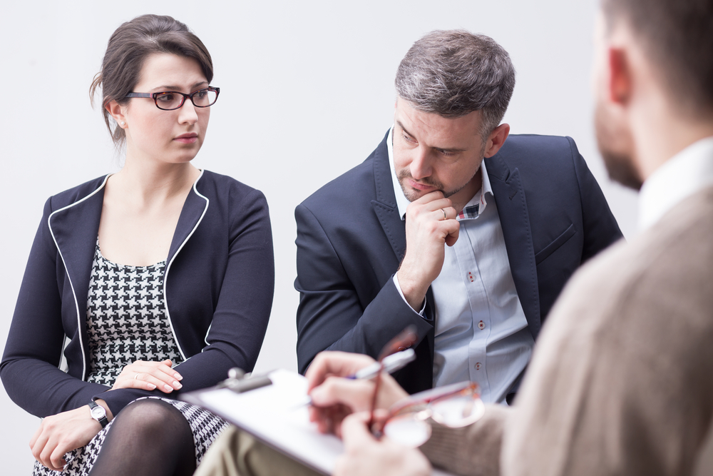 shot of an elegantly dressed couple looking angrily at each other during a conversation with a counselor