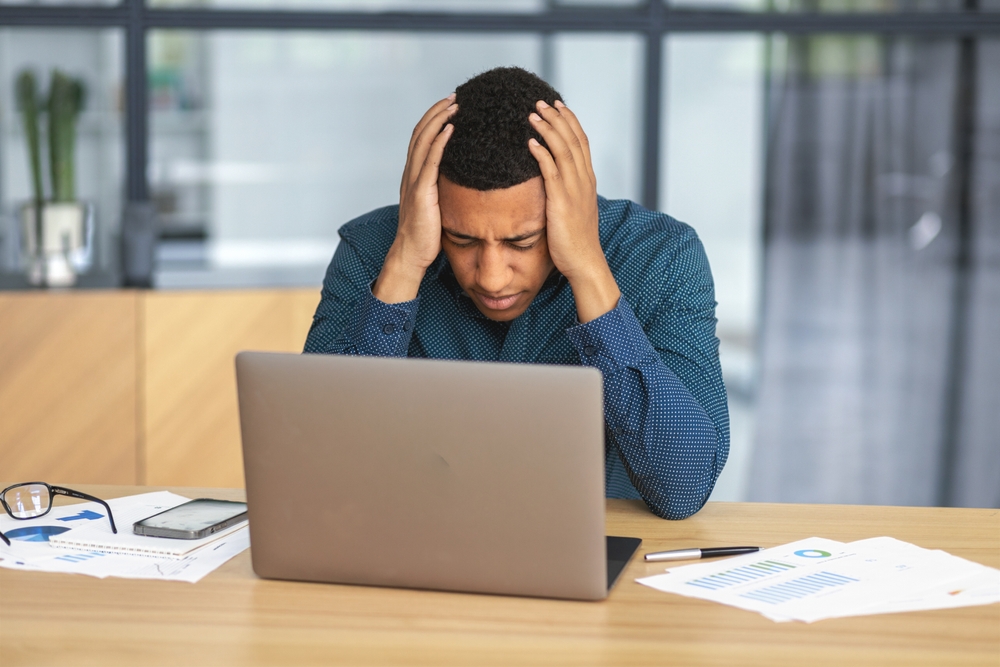 Young businessman upset by bankruptcy, covering his head with his hands sitting at the table in the office